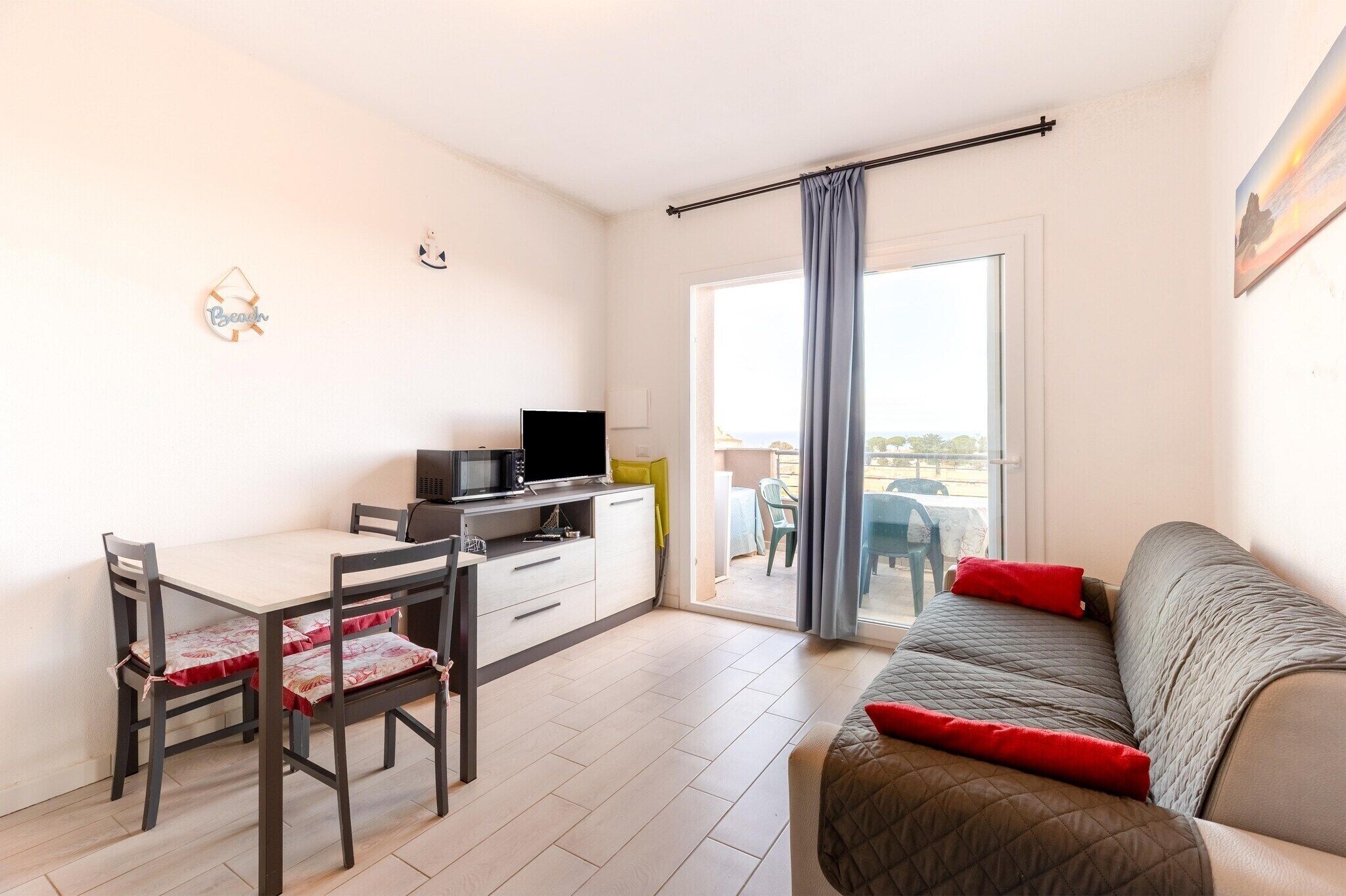 A compact living space with a kitchenette, a dining table, a sofa, and a sliding glass door leading to an outdoor area.