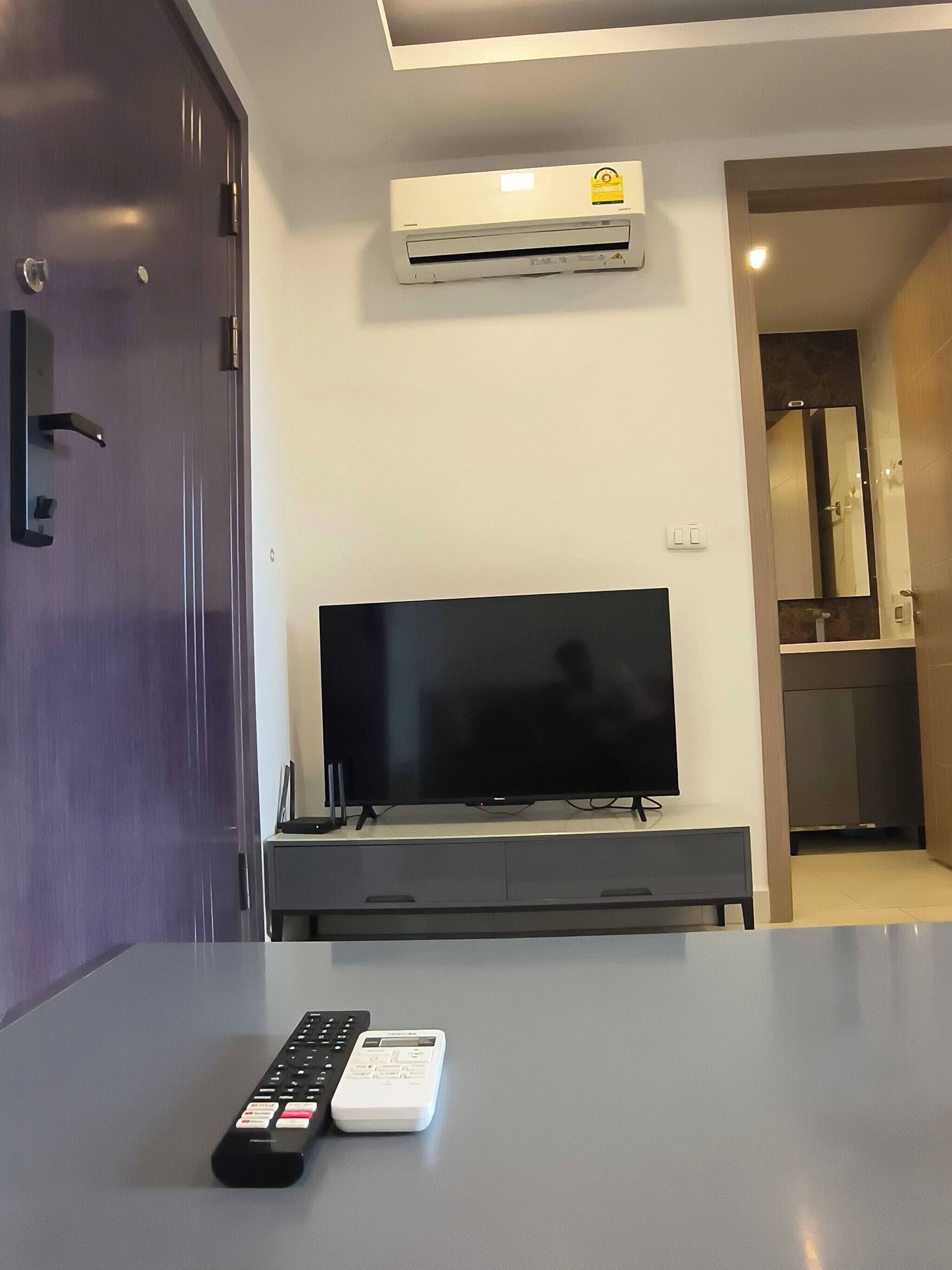 A modern living room with a flat-screen TV on a stand, a remote control, and a small white device on a table.