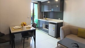 A modern kitchen with dark cabinets, a built-in oven, and a refrigerator. There is a dining area with a table and chairs, and a sofa in the living room. - Luxurious Pattaya Apartment With Pool Access (Pattaya)