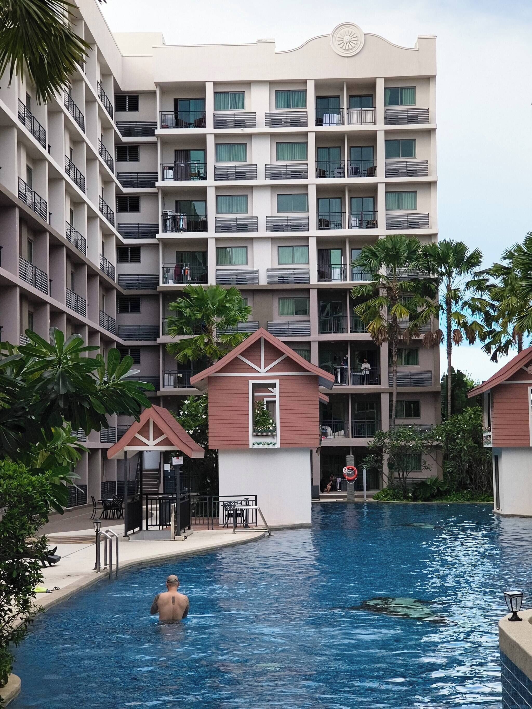 Un hôtel à plusieurs étages doté d’une piscine, de palmiers et d’un petit pavillon.