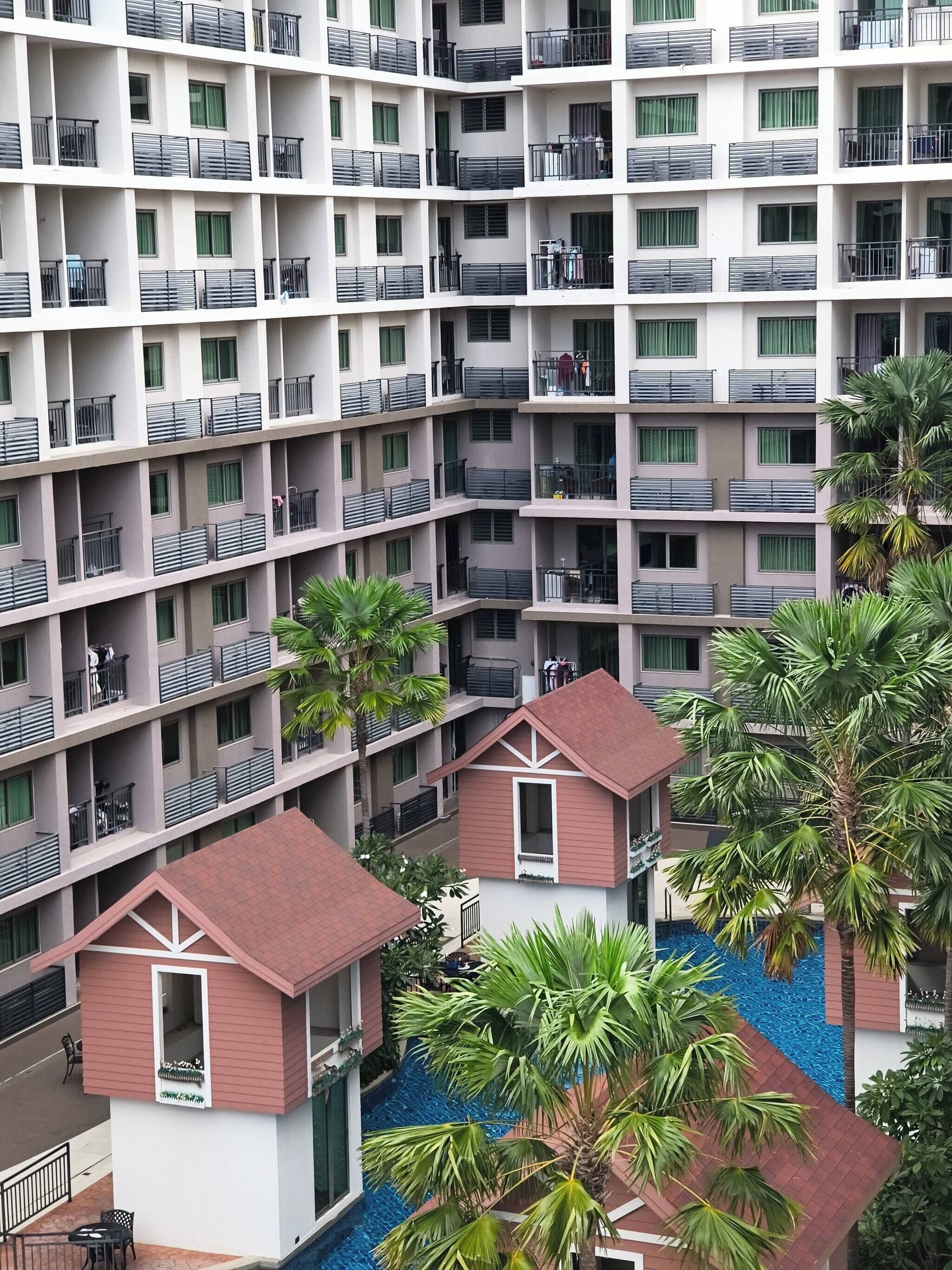 A multi-story hotel with balconies, a pool area, and palm trees.