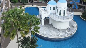 A hotel with multiple floors, a central swimming pool, and a small island with a white structure and blue dome. - Luxurious Pattaya Apartment With Pool Access (Pattaya)
