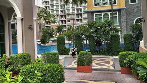 A courtyard with a swimming pool, palm trees, and a person sitting on a bench. - Luxurious Pattaya Apartment With Pool Access (Pattaya)