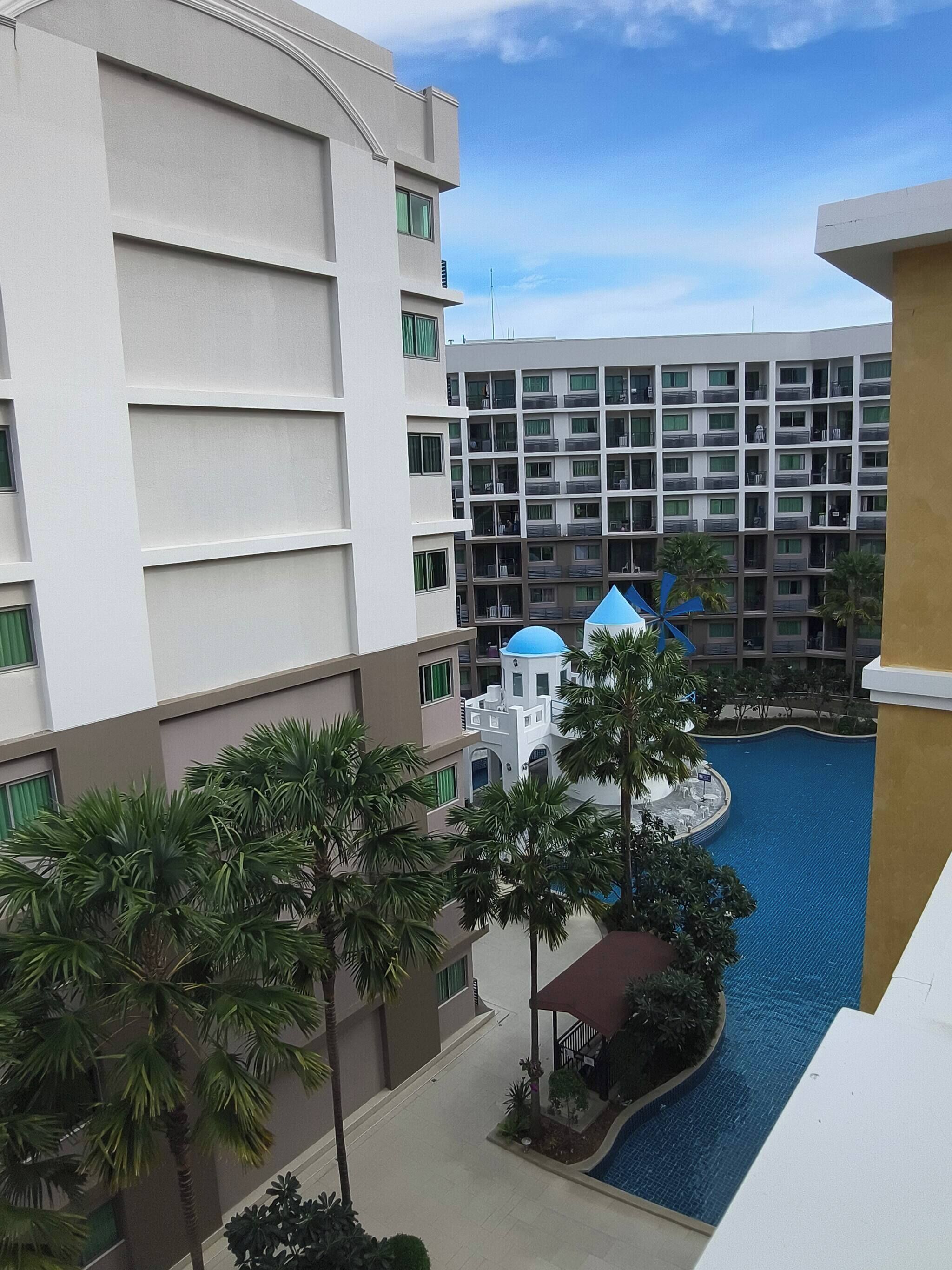 Um hotel com piscina, palmeiras e um edifício moderno com varandas.