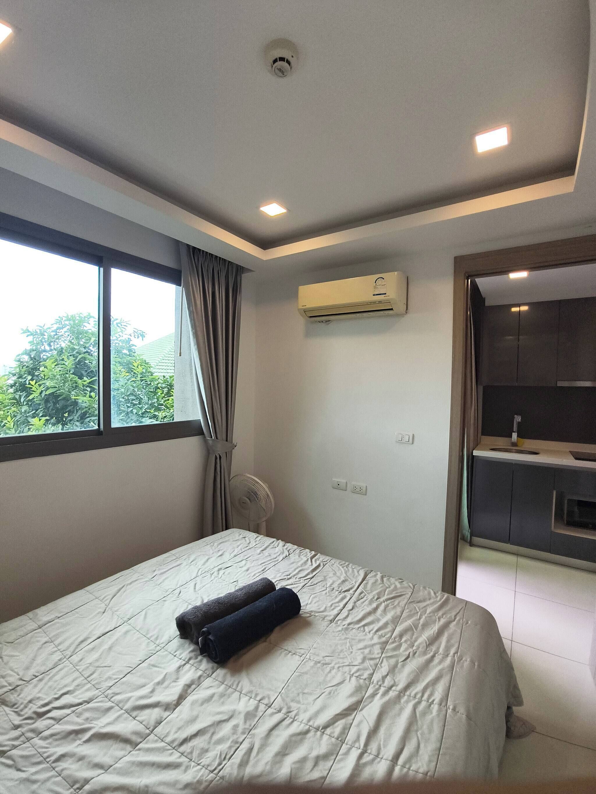 Ein modernes Schlafzimmer mit einem großen Bett, einer Klimaanlage, einem Ventilator und Blick ins Freie durch ein Fenster.