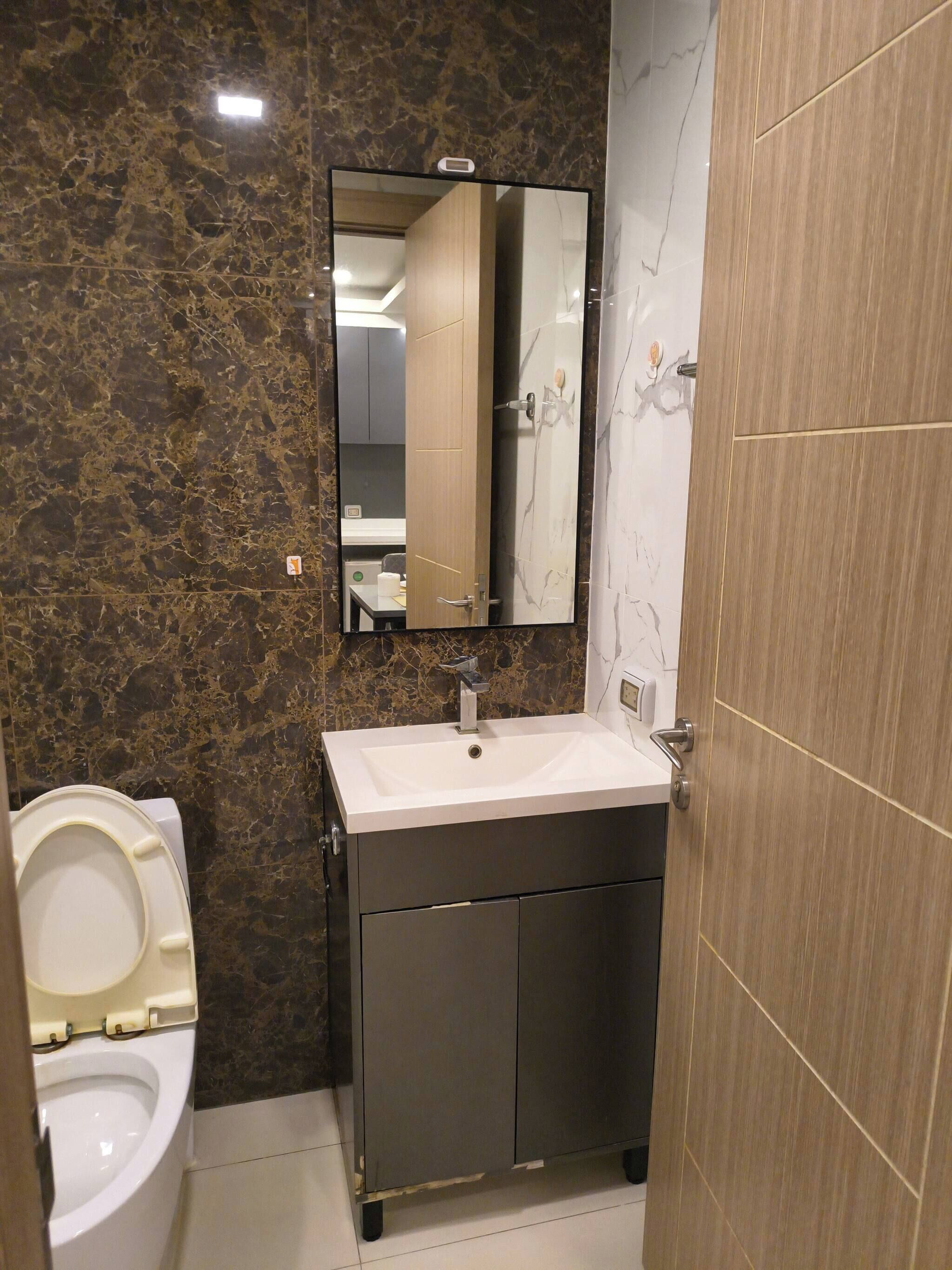 Un baño con pared de mármol, un lavabo blanco, un espejo y un inodoro.
