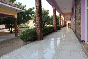 A covered corridor with tiled flooring, brick pillars, and a row of windows. - The Black Gold Hotel Lokichar (Lokichar)