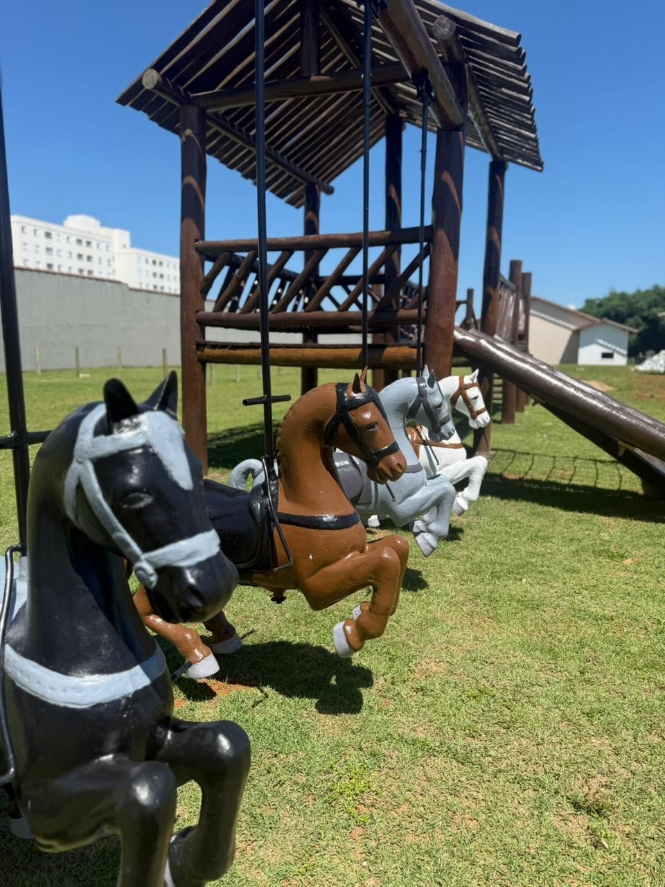 A wooden horse carousel with three horses in motion, set against a clear sky and a grassy field.