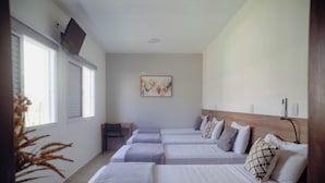 Une chambre d’hôtel avec quatre lits simples, un téléviseur à écran plat fixé au mur et une fenêtre avec des stores.
