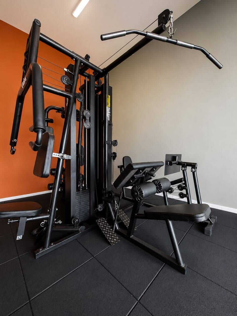 Un gimnasio con una variedad de máquinas de ejercicio, incluyendo una prensa de banca y una máquina de poleas.
