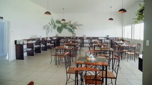 Un grand espace de salle à manger avec plusieurs tables et chaises, un comptoir de cuisine et des luminaires suspendus.