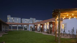 Une cour d’hôtel la nuit, avec une pelouse bien entretenue, un espace salon abrité et plusieurs bâtiments dont les fenêtres sont illuminées.