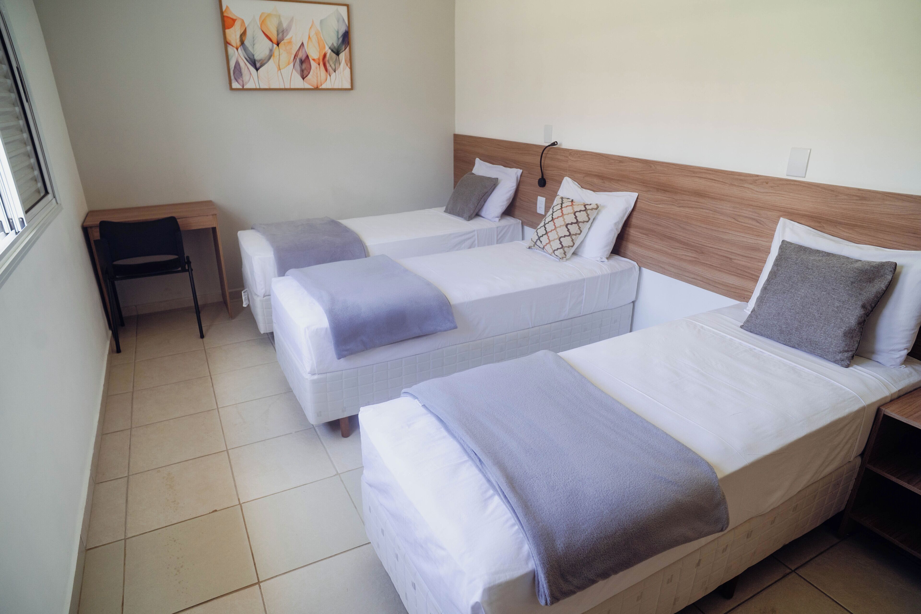 Habitación de hotel con tres camas individuales, una mesita y una obra de arte colgada en la pared.