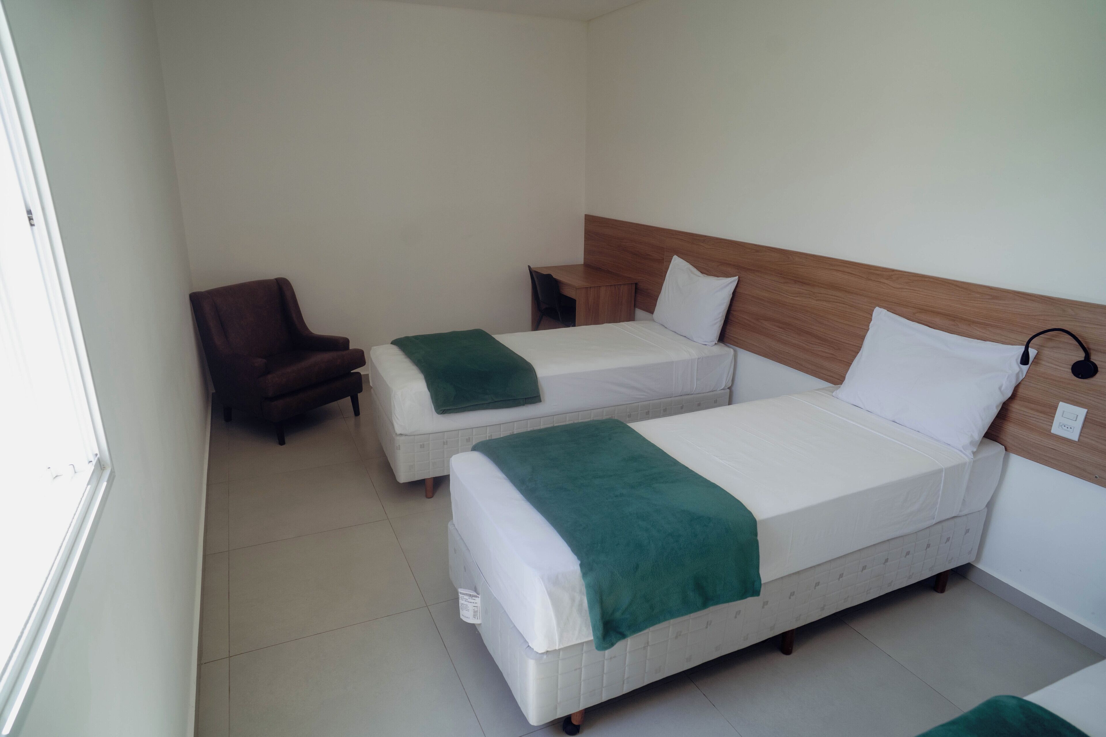 A hotel room with two beds, a chair, and a desk.