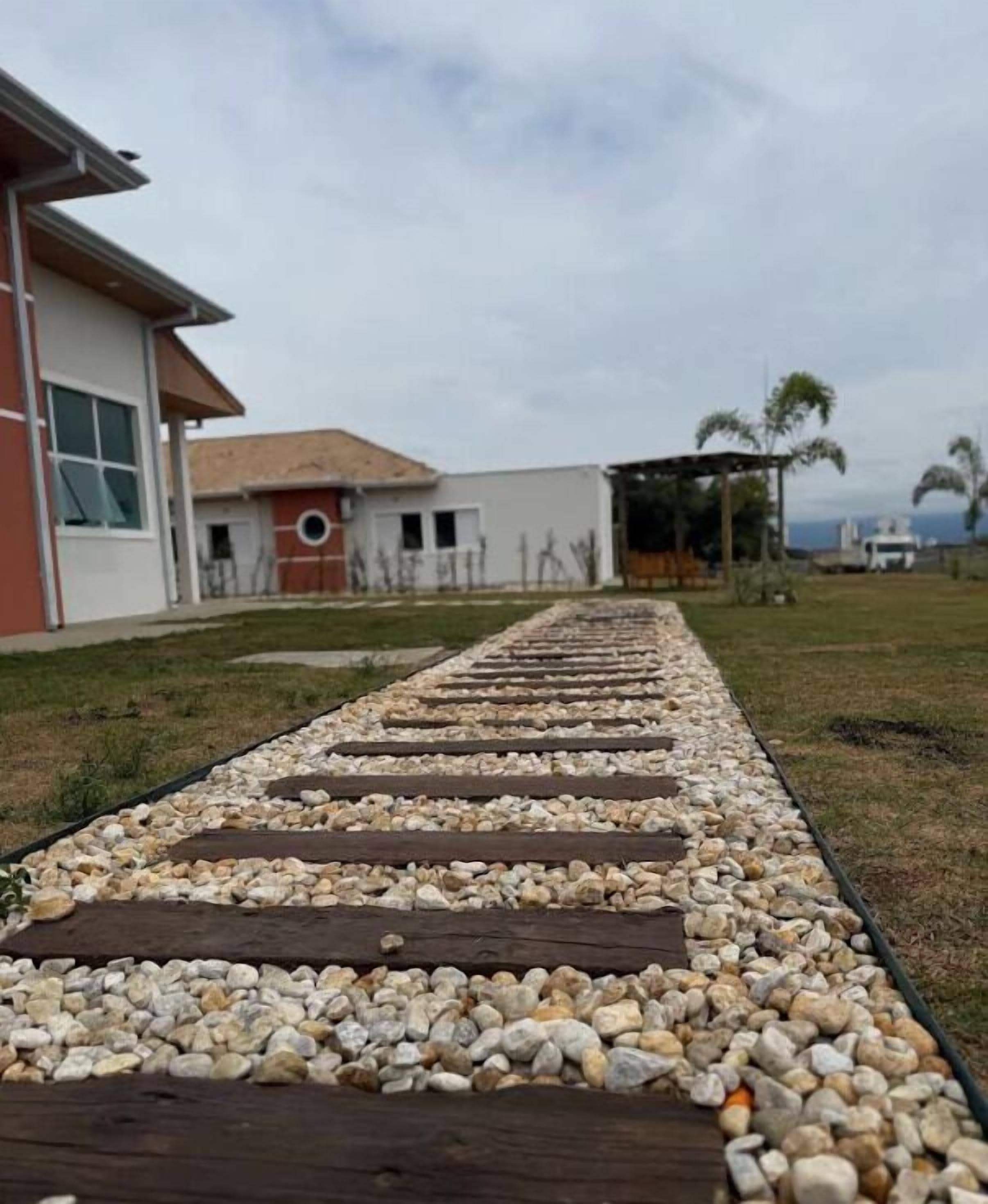 Ein Weg mit Holzdielen und Kieselsteinen führt zu einem Gebäude mit roter und weißer Fassade.