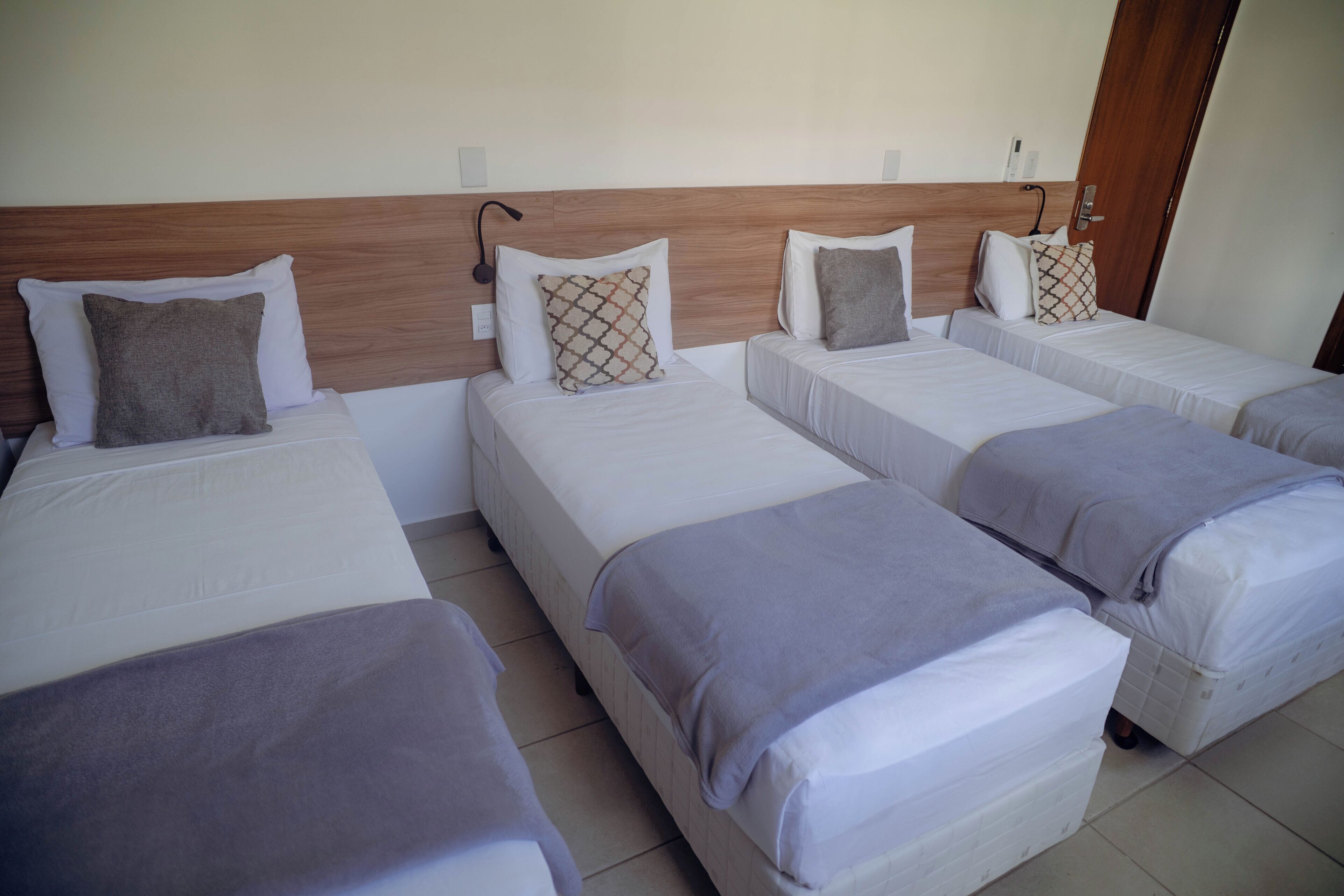 Quarto de hotel com quatro camas individuais, cada uma com travesseiro e cobertor.