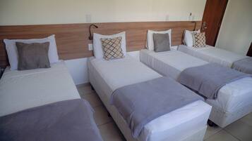 Quarto de hotel com quatro camas individuais, cada uma com travesseiro e cobertor.