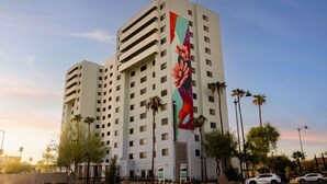 A multi-story hotel with a large mural on the side, palm trees, and a clear sky. - Solstice Haven - Desert Sky Getaway (Mesa)