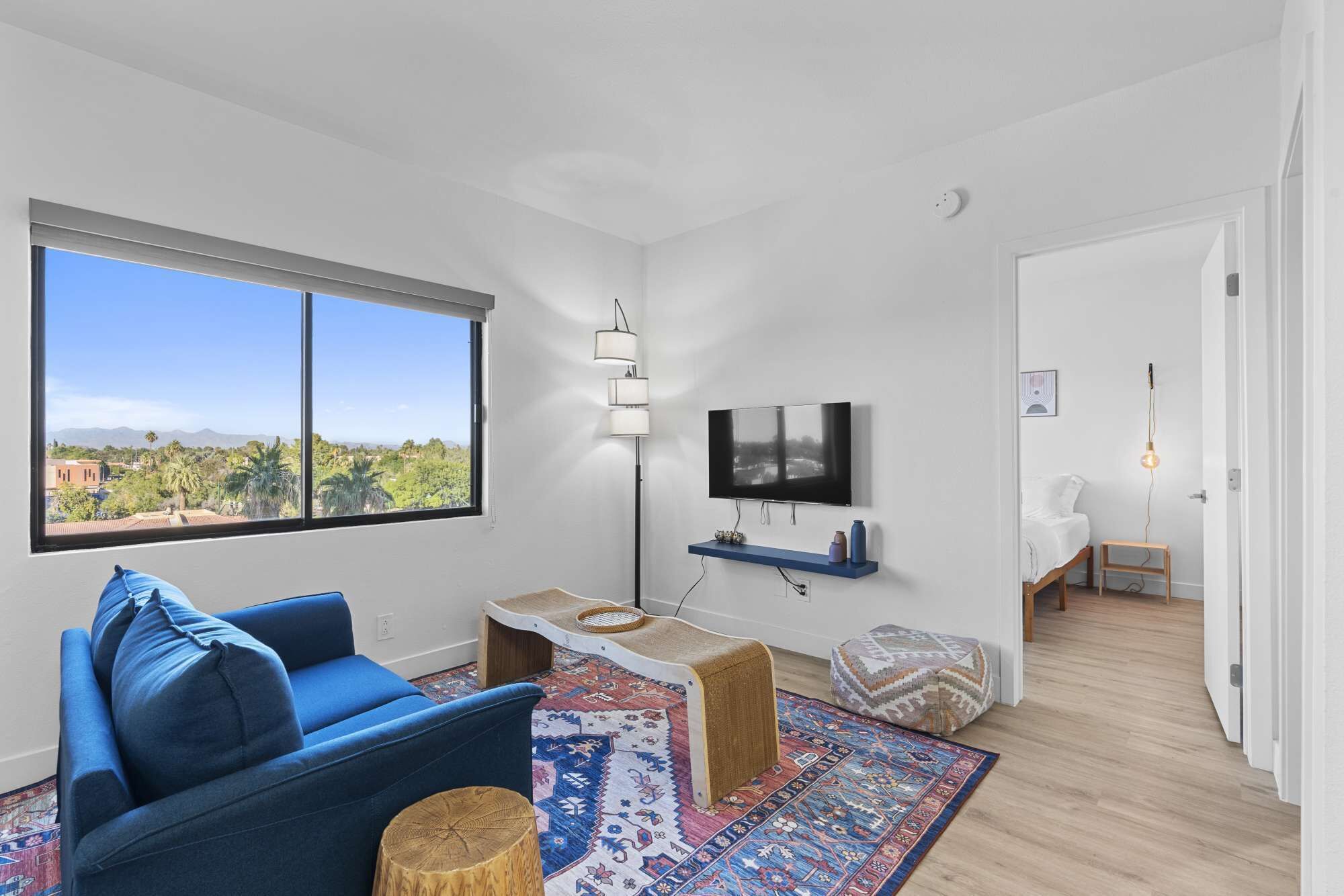 A modern living room with a large window, a blue sofa, a TV, and a small table.