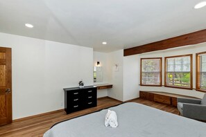 Ein Schlafzimmer mit einem Bett, einem Schminktisch, einer Bank und einem Fenster mit Jalousien.
