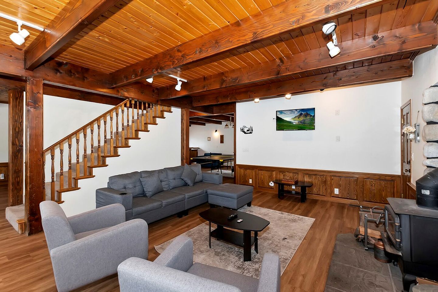 A spacious living room with a wooden staircase, a gray sectional sofa, a small table, and a fireplace.