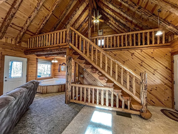 A log cabin interior with a wooden staircase, a hot tub, and a cozy seating area. - Beautiful Cabin Suitable for Families with Back Porch in Ohio (Millersburg)