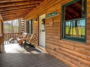 A log cabin with a porch, wooden chairs, a sign reading 'COZY PINE,' and a view of trees through the window. - Beautiful Cabin Suitable for Families with Back Porch in Ohio (Millersburg)