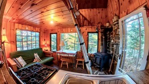 Interior acogedor de una cabaña con un sofá verde, una mesa de comedor, una estufa y una chimenea de piedra.