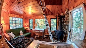 Interior acogedor de una cabaña con un sofá verde, una mesa de comedor, una estufa y una chimenea de piedra.