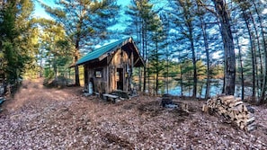 Una cabaña rústica con techo de metal, rodeada de un bosque y un lago.