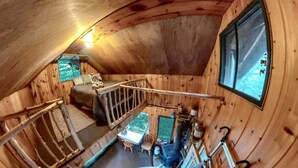 Un interior de madera con una escalera, una mesa, sillas y un ventanal.