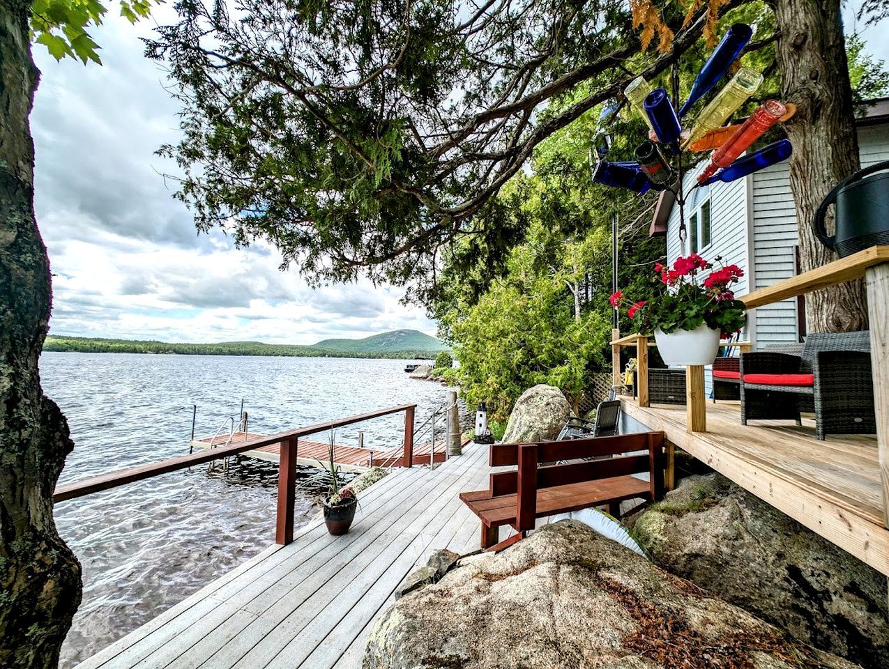 A wooden deck with a bench and potted plants, overlooking a body of water with a dock.