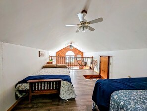 Une chambre avec deux lits, un ventilateur de plafond et un plancher en bois.