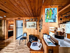 L’intérieur chaleureux d’un chalet avec un plafond en bois, un coin repas comprenant une table et des chaises, une cuisine dotée de meubles en bois et un tableau accroché au mur.