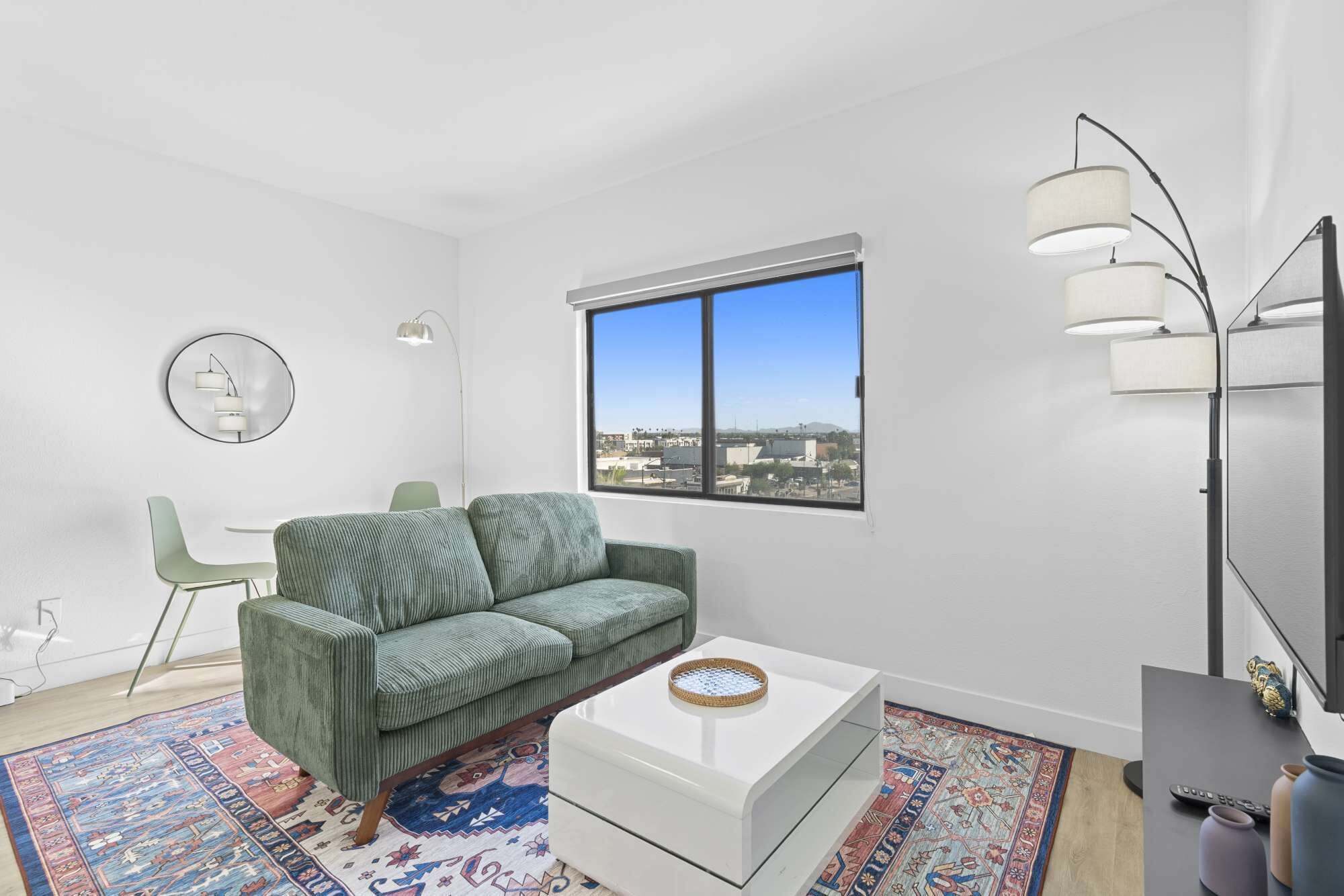 Una sala de estar moderna con un sofá verde, una mesa de centro blanca y un amplio ventanal con vistas a la ciudad.