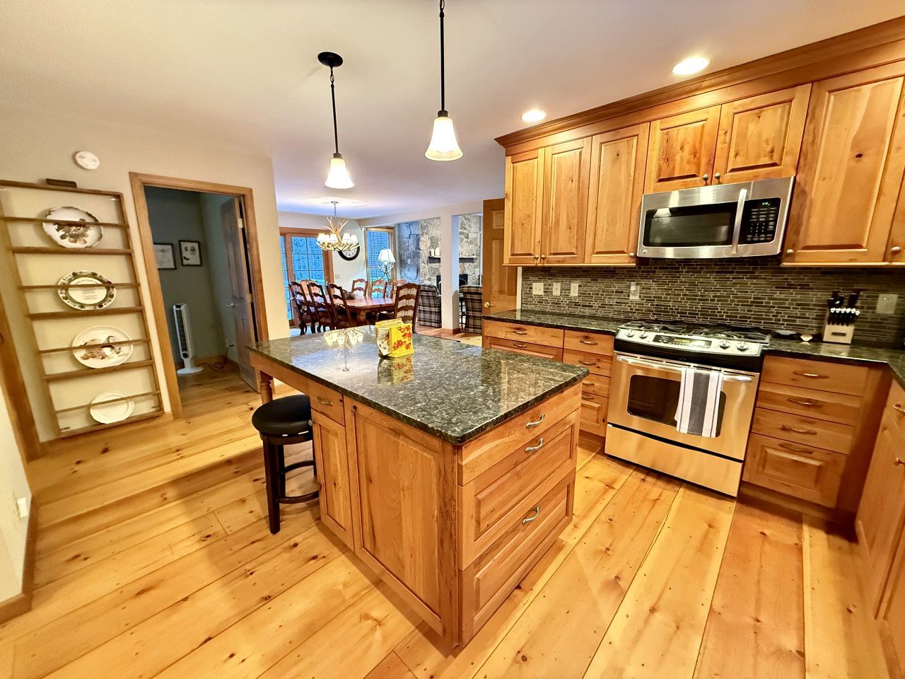 A kitchen with wooden cabinets, a granite countertop, stainless steel appliances, and a central island with bar stools.