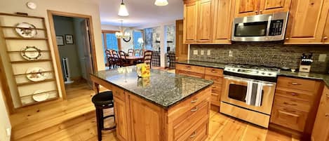 A kitchen with wooden cabinets, a granite countertop, stainless steel appliances, and a central island with bar stools.