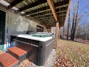 A hot tub under a wooden roof, surrounded by trees.