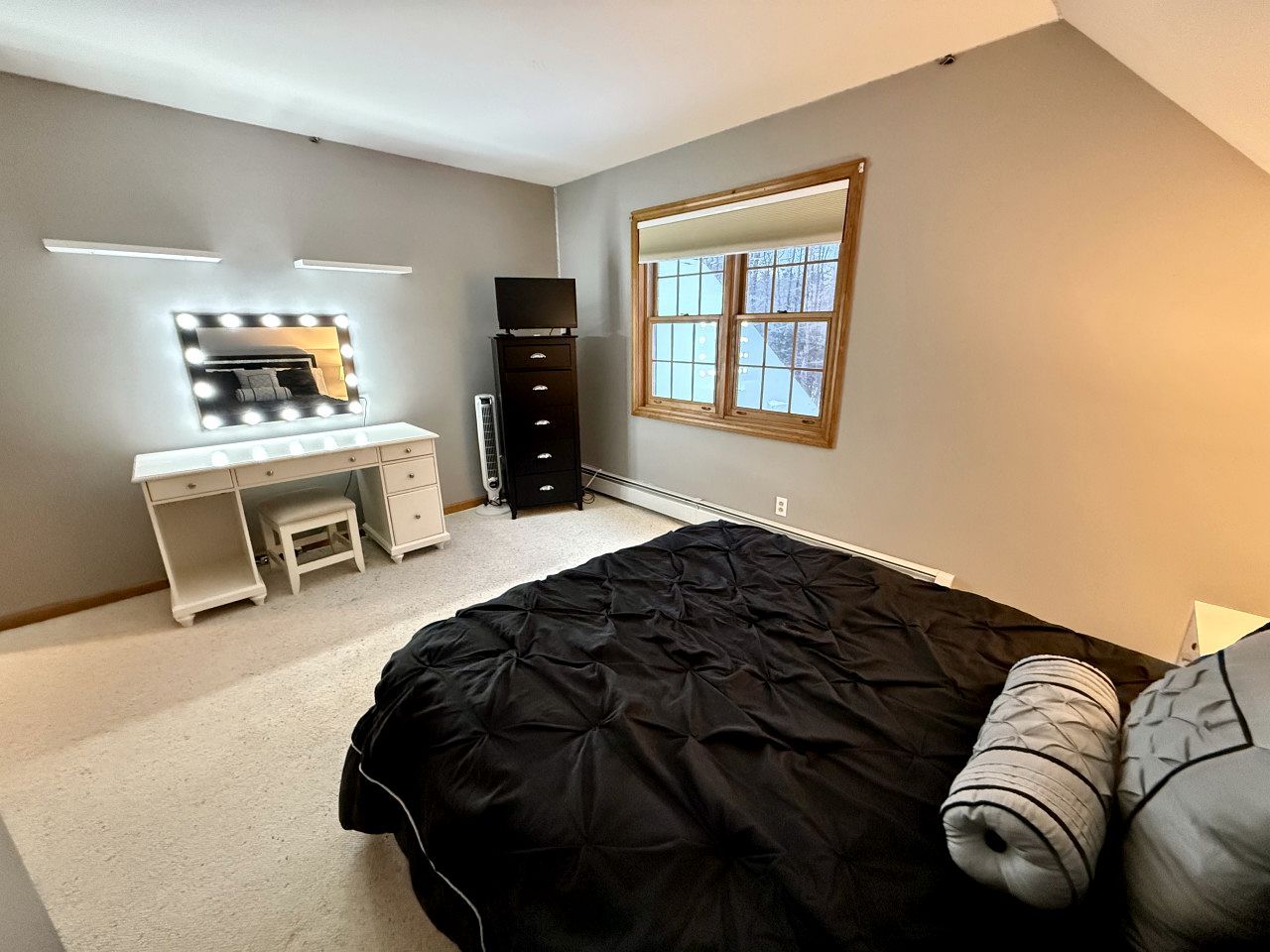 Une chambre à coucher avec un lit, un bureau doté d’un miroir, une commode et une fenêtre.