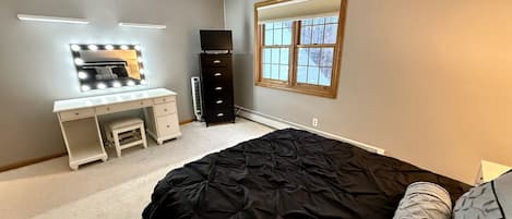 Une chambre à coucher avec un lit, un bureau doté d’un miroir, une commode et une fenêtre.