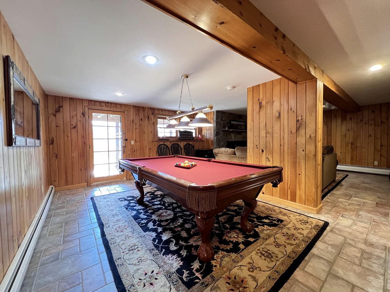 A pool table in a room with wooden walls and a stone fireplace.