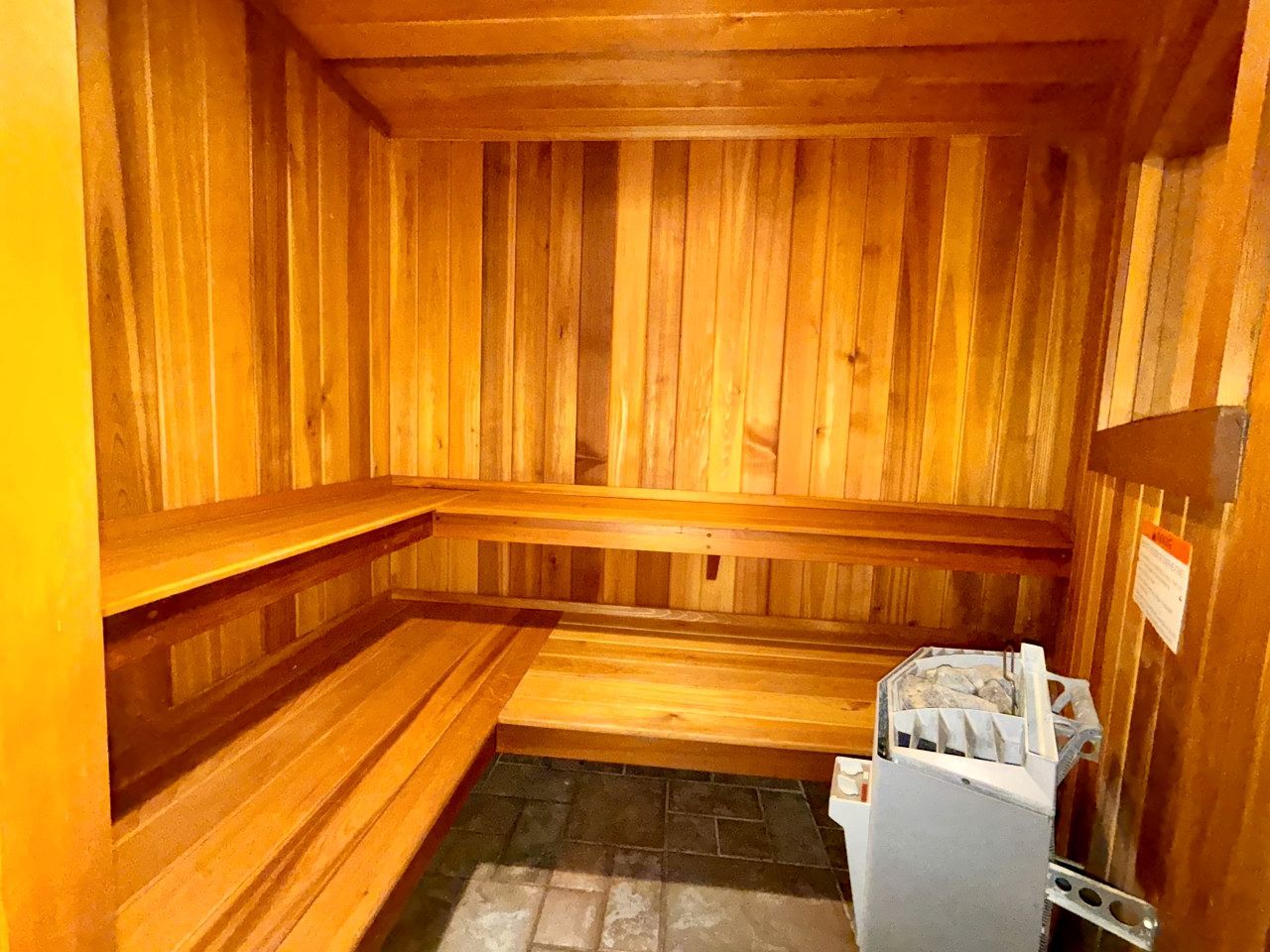A sauna with wooden walls and benches, a tiled floor, and a sauna heater.