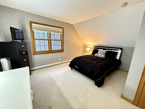 Ein Schlafzimmer mit Bett, Kommode, Fenster und Heizung.