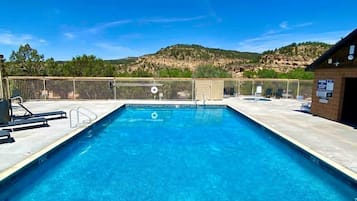 A rectangular swimming pool with clear blue water, surrounded by a fence, and a building with a brick exterior to the right.