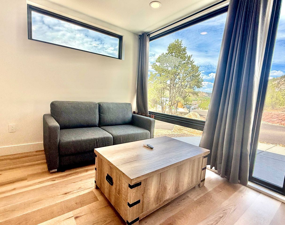 Un salon moderne avec un canapé gris, une table basse en bois et de grandes fenêtres ornées de rideaux.