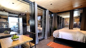 A modern bedroom with a large bed, a dining area with a table and chairs, and a view through a glass door. - Chic Tiny House with Outdoor Espace to Relax in Orderville, Utah (Orderville)