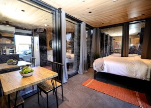 Une chambre moderne avec un grand lit, un coin repas comprenant une table et des chaises, et une vue à travers une porte vitrée.
