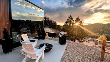 An outdoor patio with white chairs, a fire pit, and a grill.