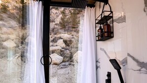A modern bathroom with a shower, white curtains, and a view of rocky terrain. - Chic Tiny House with Outdoor Espace to Relax in Orderville, Utah (Orderville)