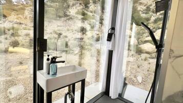 Un baño con lavamanos, espejo y ventana con vista a un paisaje rocoso.